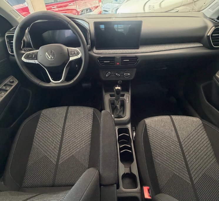 Interior moderno y tecnológico del Volkswagen Tera Comfort. Destaca el volante multifunción con el emblema de VW, el sistema de infoentretenimiento con pantalla táctil flotante y el tapizado de tela bitono en los asientos con diseño de chevron. La consola central alberga la palanca de cambios automática y espacio para posavasos.