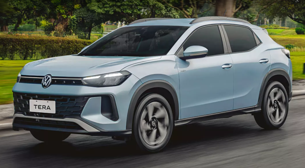 Vista de tres cuartos de un SUV Volkswagen Tera Comfort color azul celeste claro circulando por una calle. Se aprecian las luces LED encendidas, la parrilla frontal con el logo de VW y la placa 'TERA', además de un fondo con árboles y vegetación.