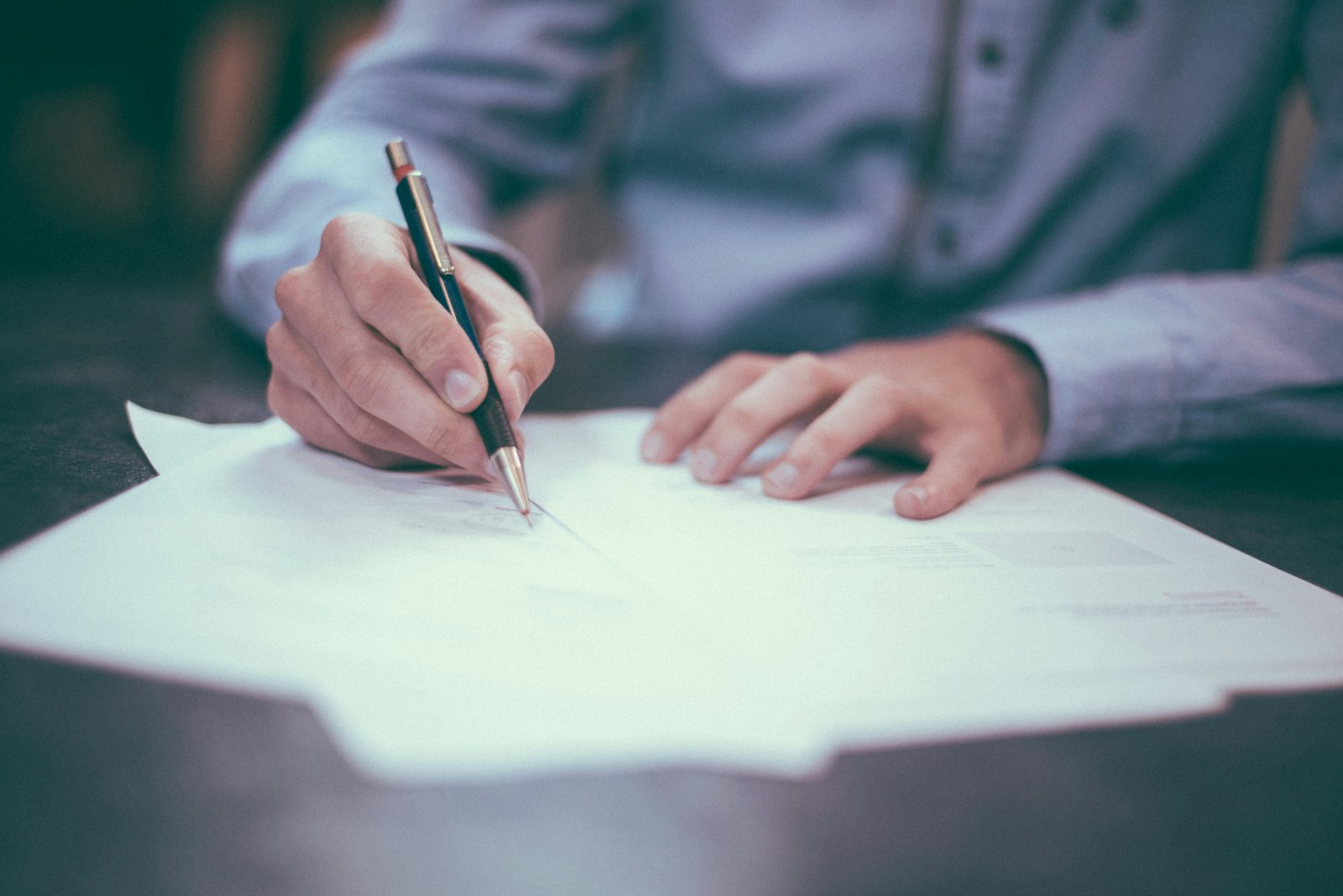 Persona firmando la documentación y los papeles de transferencia para la compra de un auto usado.
